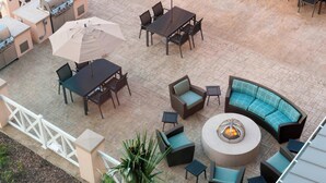 Un espace extérieur aménagé avec un barbecue, des tables à manger, des chaises et un foyer.