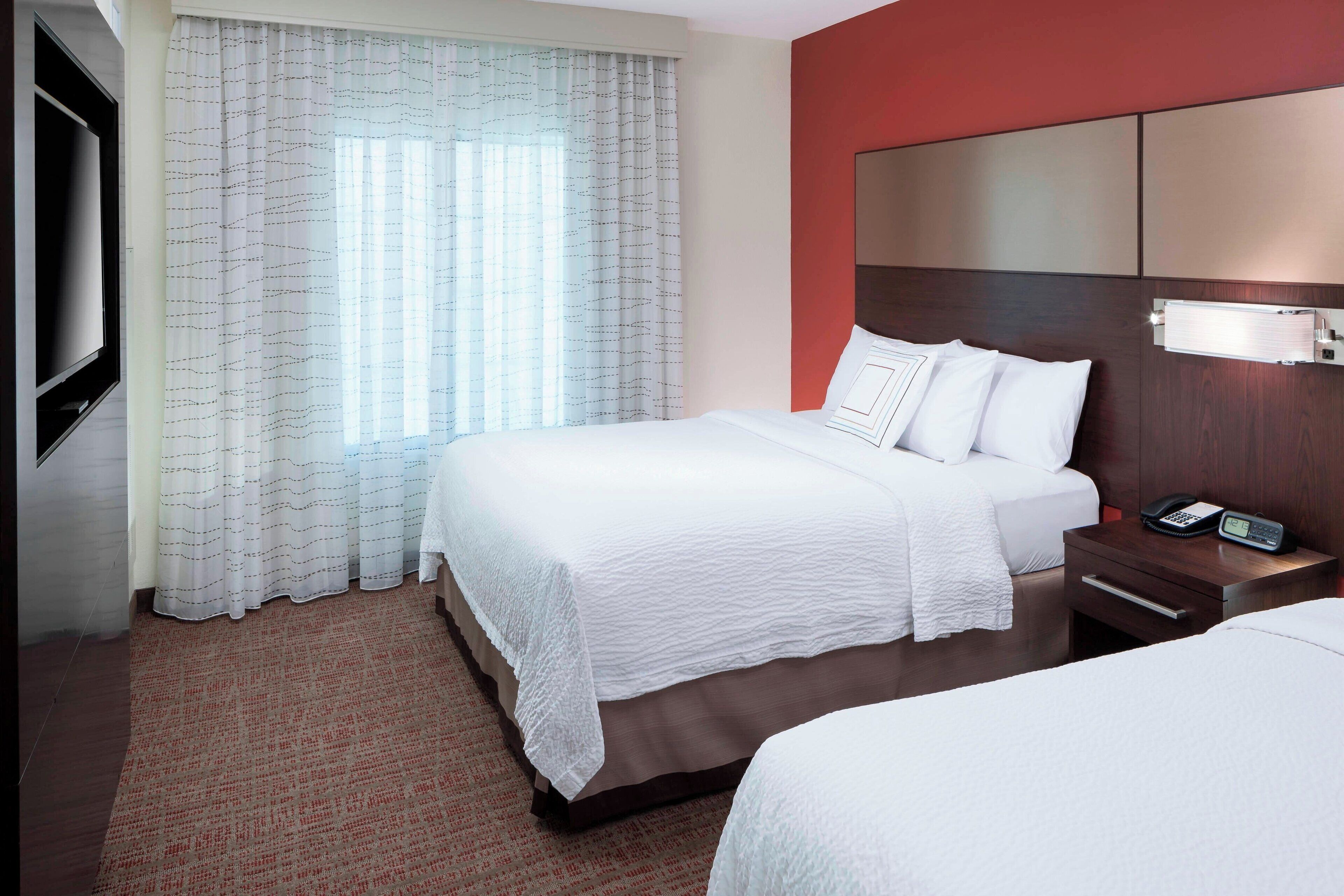 Quarto de hotel com uma cama grande, mesa de cabeceira com telefone e televisão na parede.