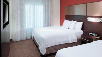 Quarto de hotel com uma cama grande, mesa de cabeceira com telefone e televisão na parede.