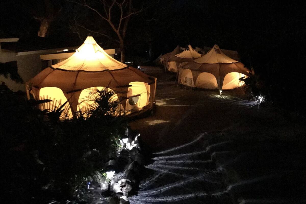 A series of dome-shaped tents with a central light source, surrounded by trees and a pathway.