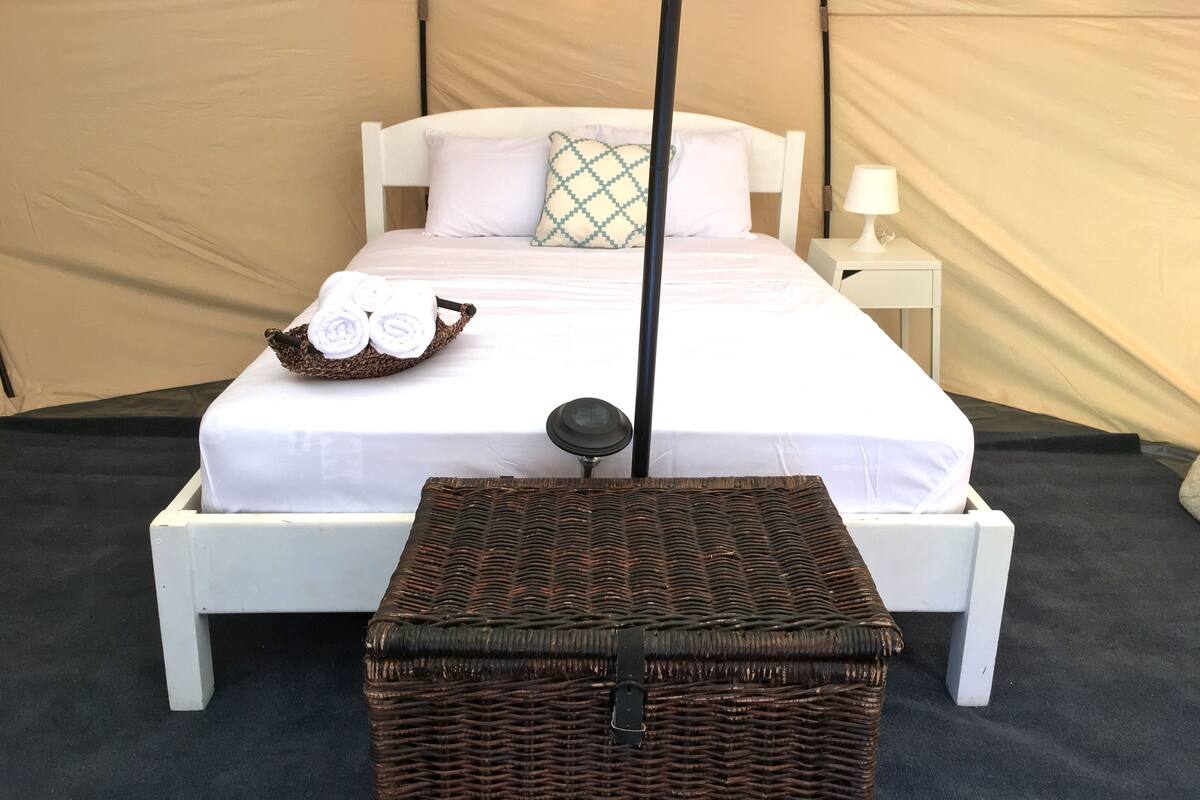 A bed with white bedding, a bedside table with a lamp, and a wicker basket with towels.
