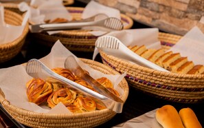 A buffet table with baskets of pastries and bread, and serving tongs. - Kilimanjaro Wonders Hotel (Moshi)