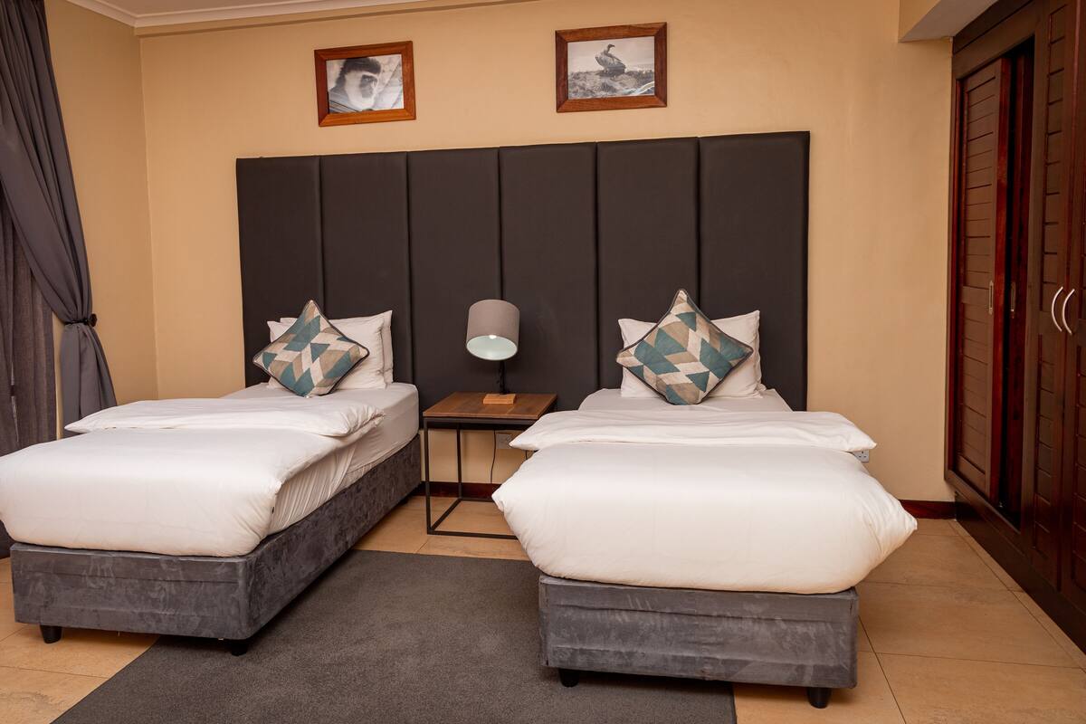 Een hotelkamer met twee bedden, een nachtkastje, een lamp en een garderobe.