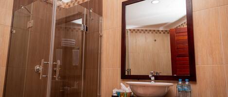 A modern bathroom with a glass-enclosed shower, a large mirror, and a sink with toiletries.