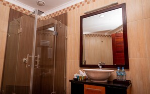 A modern bathroom with a glass-enclosed shower, a large mirror, and a sink with toiletries. - Kilimanjaro Wonders Hotel (Moshi)