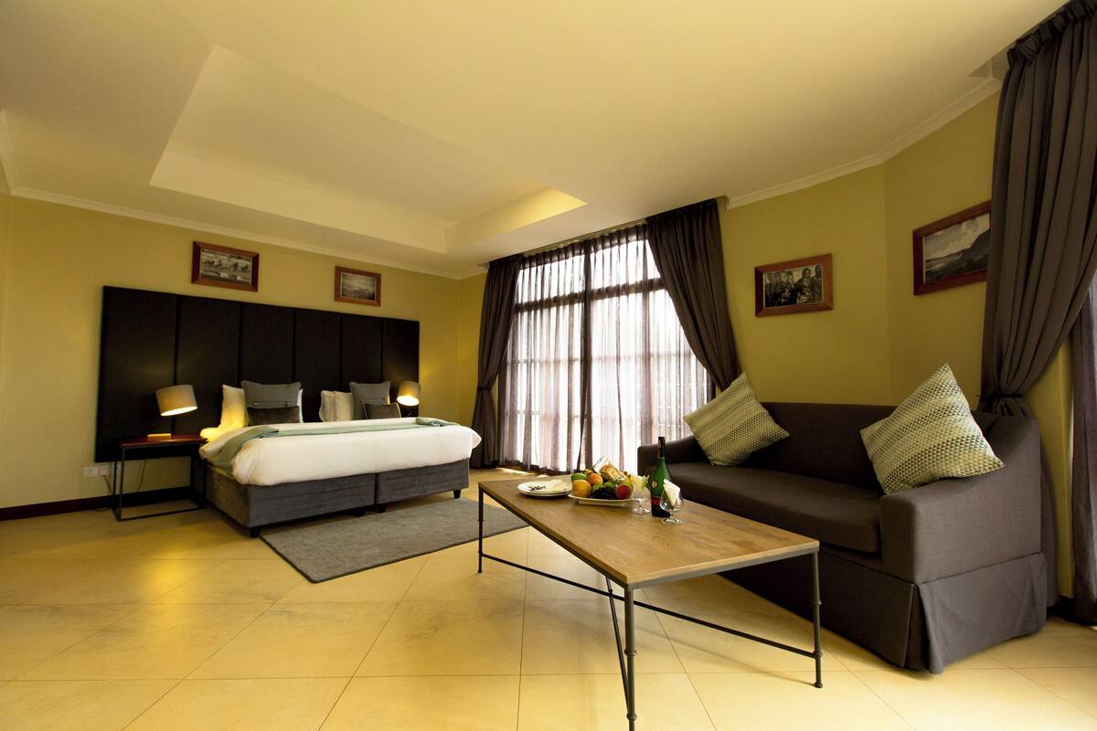 Een hotelkamer met een bed, een slaapbank, een bijzettafeltje en een groot raam met gordijnen.