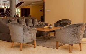A modern living room with a sofa, two armchairs, a coffee table, and a staircase in the background. - Kilimanjaro Wonders Hotel (Moshi)