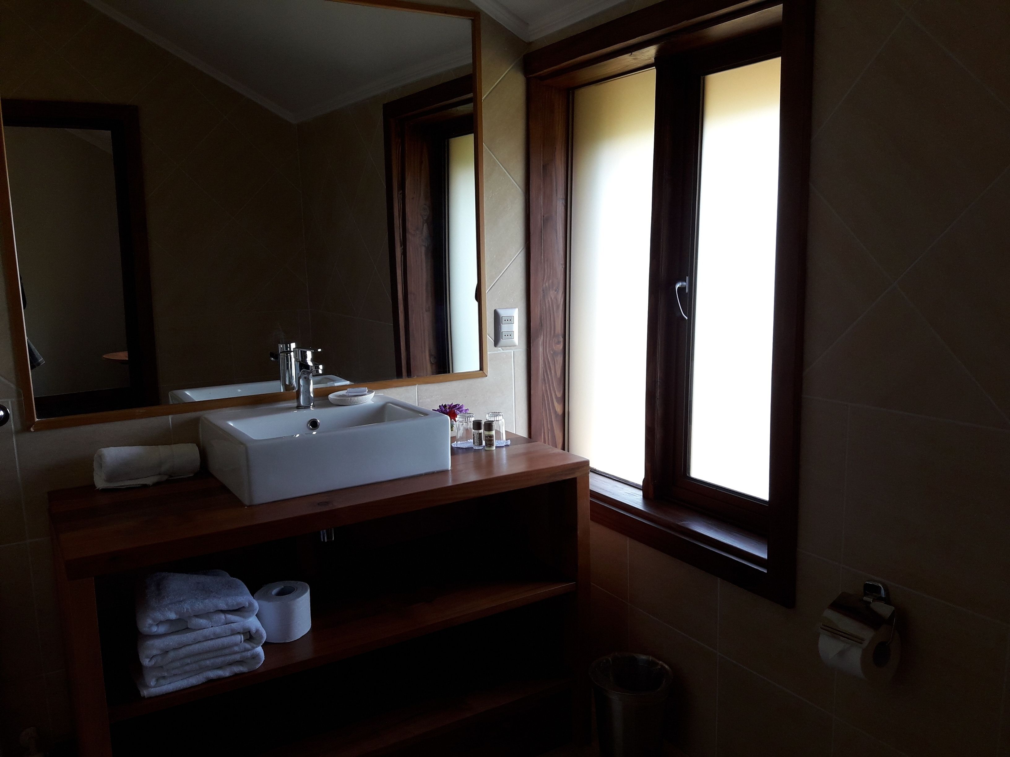 A bathroom with a large mirror, a white sink, a wooden vanity, towels, and a window with curtains.