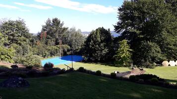 Un jardín bien cuidado con una piscina azul, rodeado de abundante vegetación y árboles.