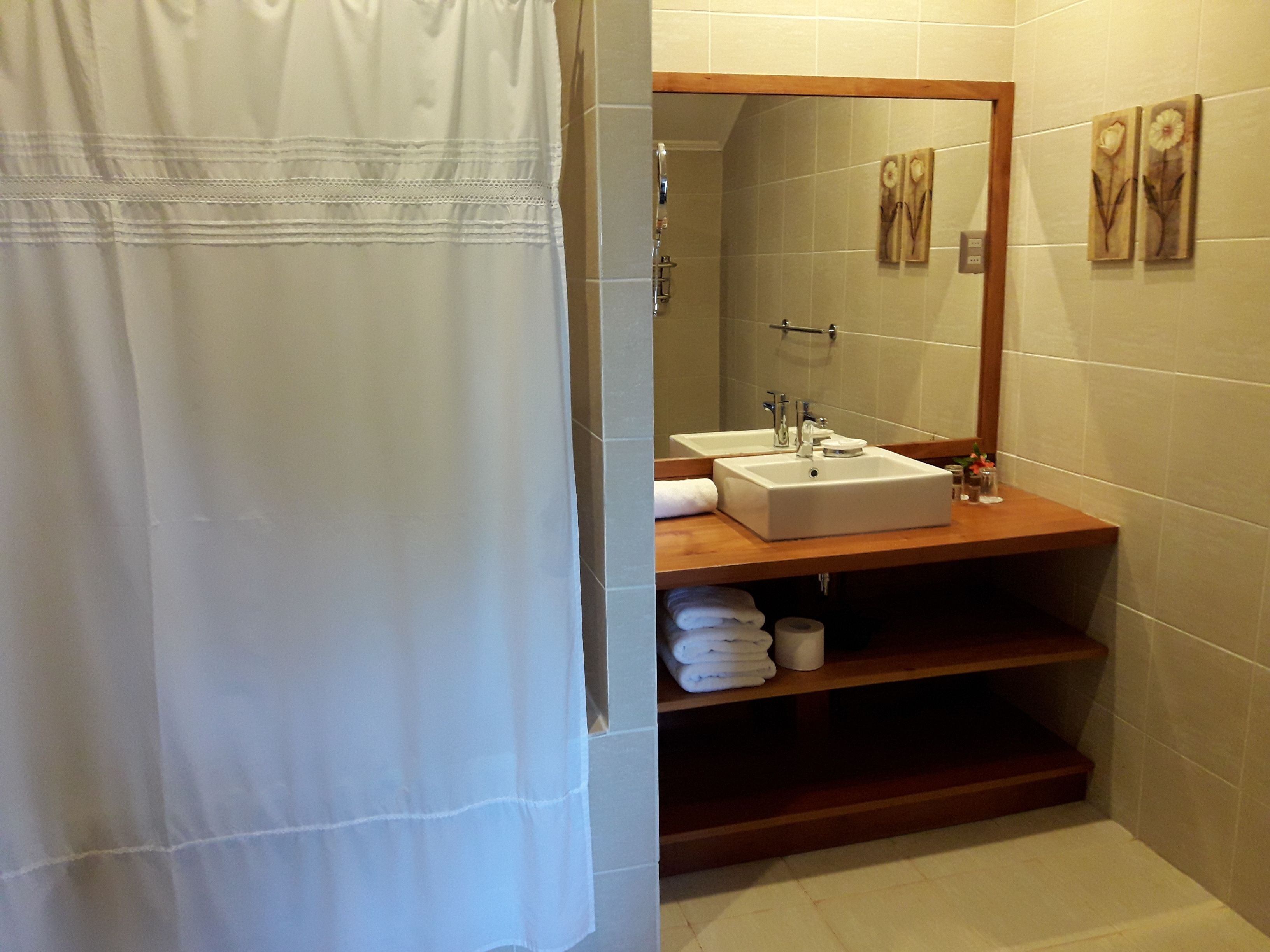 A bathroom with a wooden vanity, a white sink, a mirror, and a shower curtain.