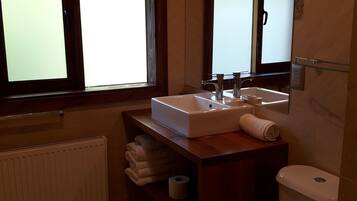 A modern bathroom with a white sink, a toilet, and a window with frosted glass.