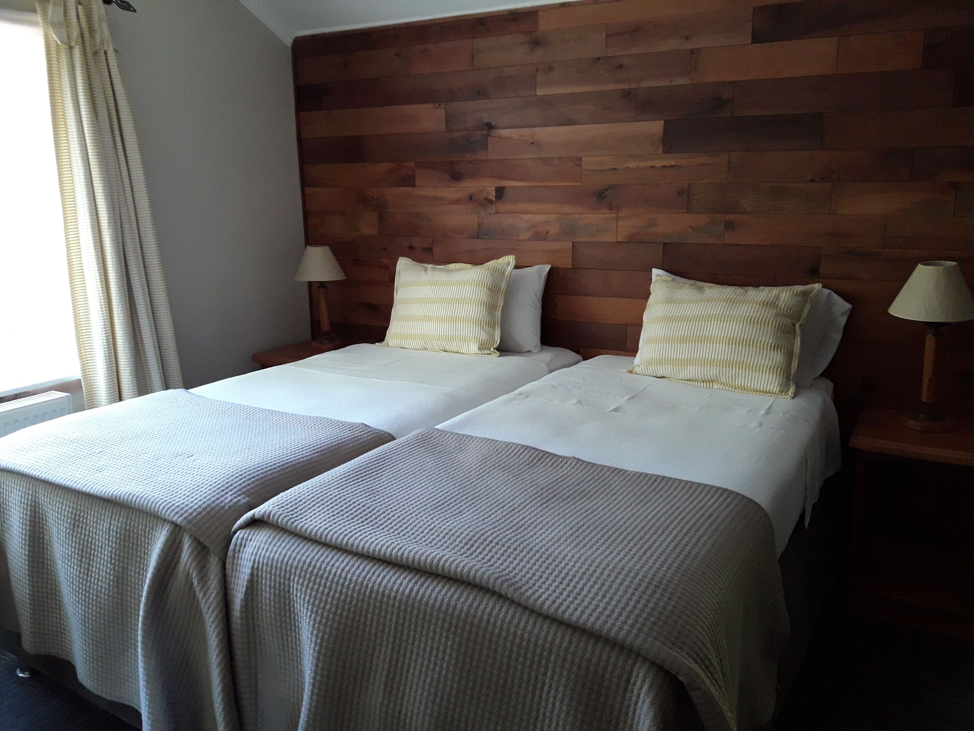 A double room with two beds, wooden headboard, bedside lamps, and a window with curtains.