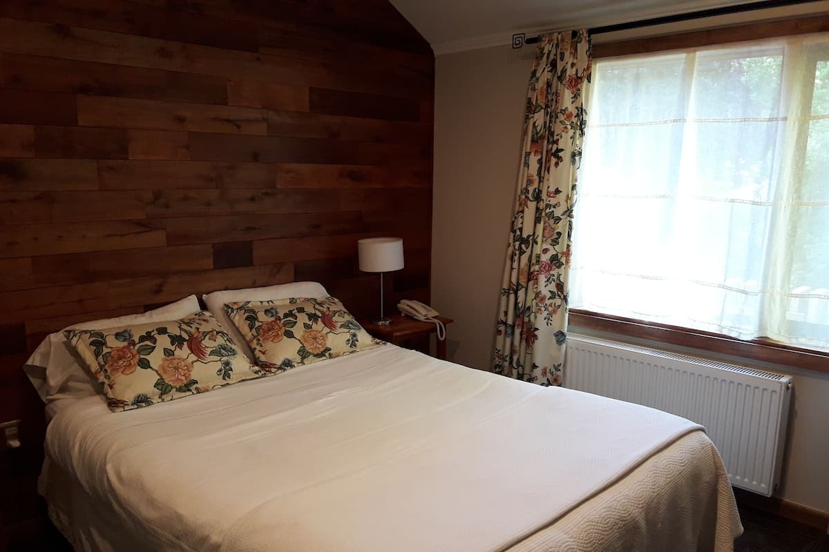 Una cama bien hecha con almohadillas florales, una lámpara de noche y un teléfono sobre un cabecero de madera.