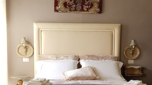 A neatly made bed with pillows and folded towels, a round table with a chair, and a patterned rug on the floor.