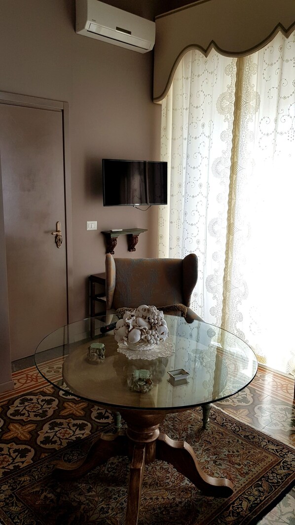 Una sala de estar con una mesa de vidrio, un sofá, un televisor montado en la pared y un tapete estampado.