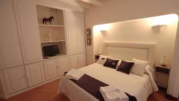 A neatly arranged bedroom with a bed, a television on a shelf, and a bedside table with a lamp.