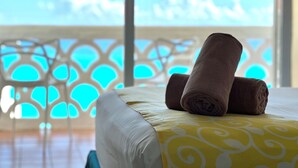 A bed with rolled towels and a yellow patterned bedspread, a white chair, and a balcony with a view of the sea. - Ocean View Apartments (Cancun)