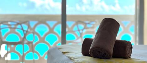 A bed with rolled towels and a view of a blue sky through a window.