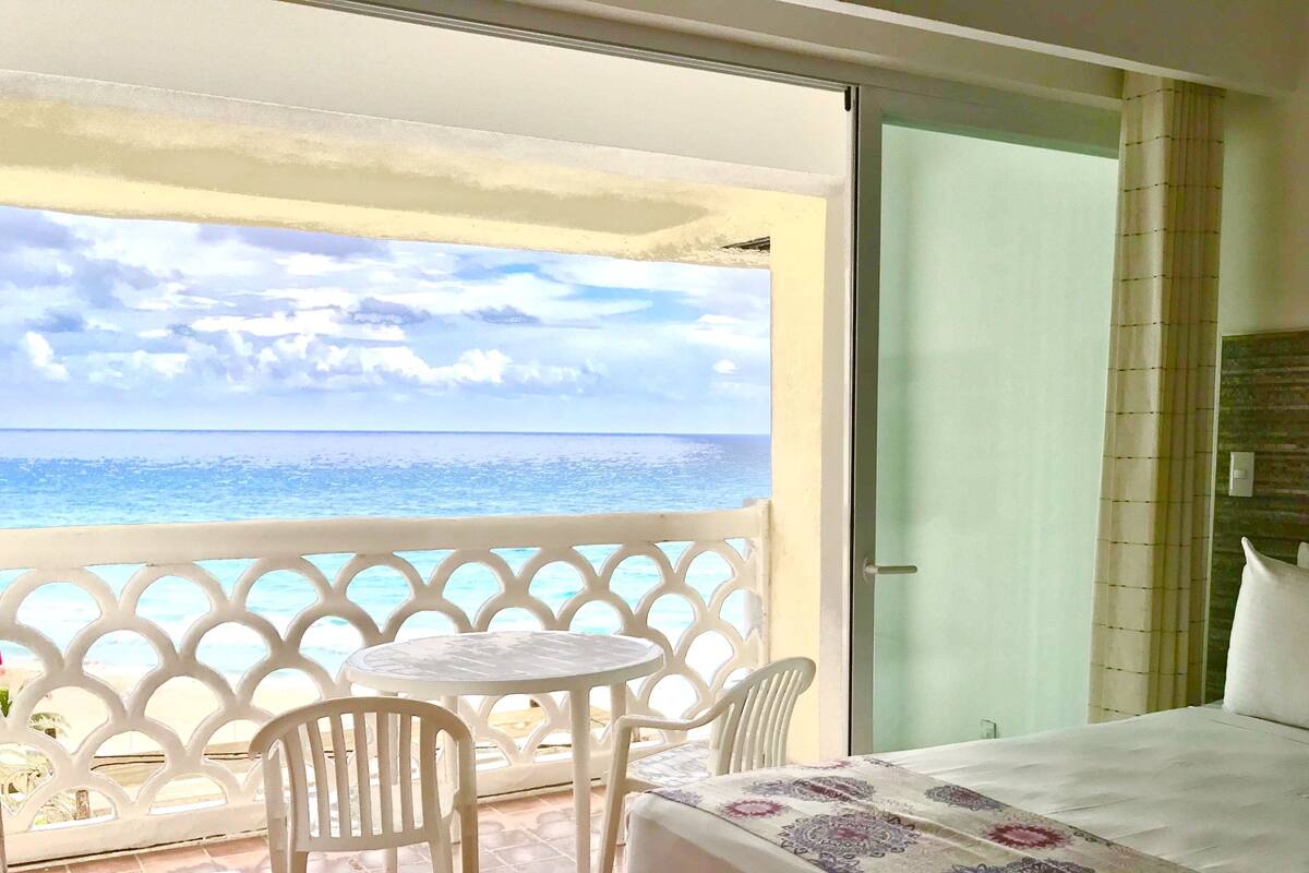 Habitación de hotel con balcón, cama con colcha estampada y vista al mar.