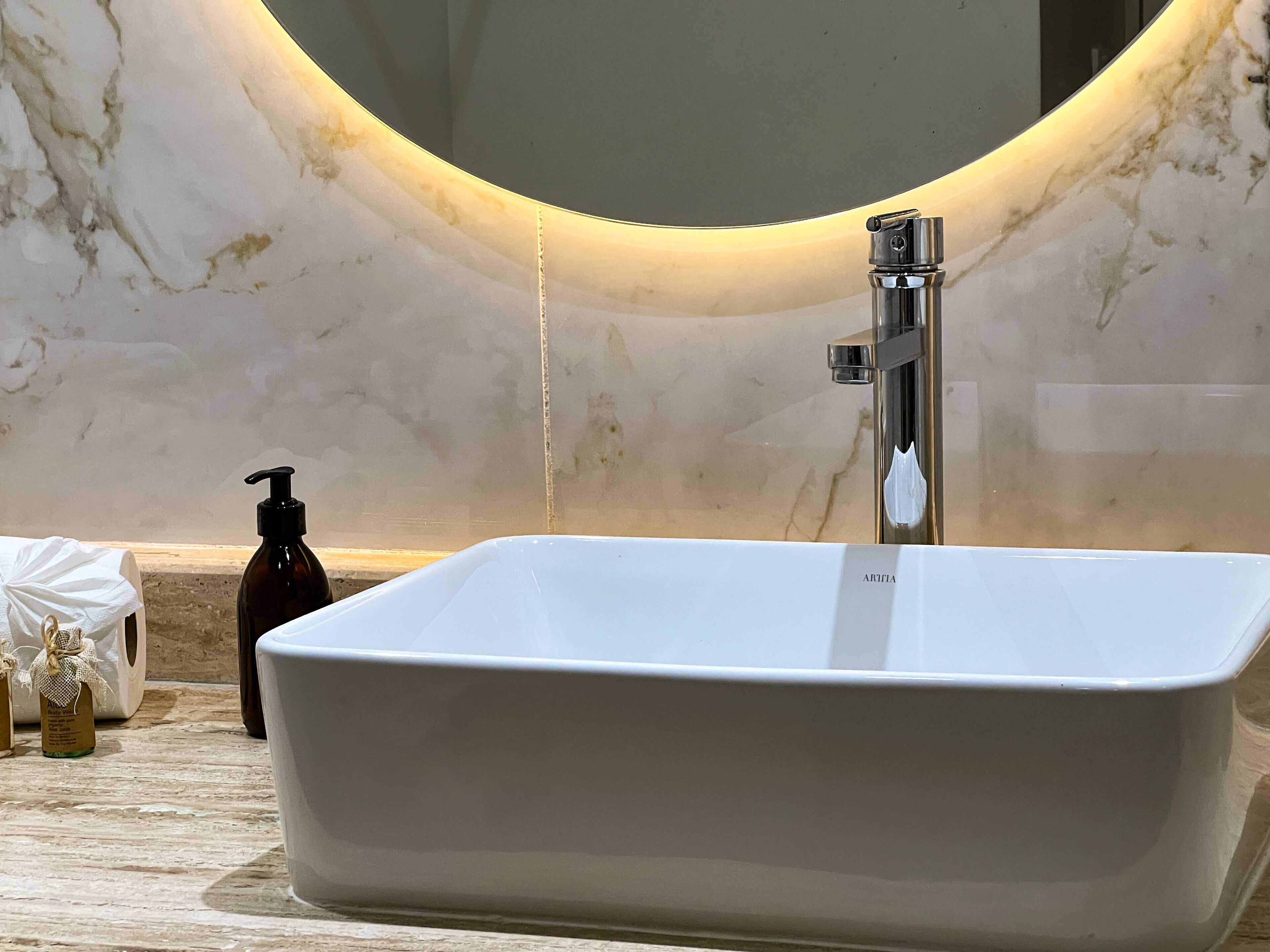 A bathroom with a rectangular white sink, a chrome faucet, and a large mirror with a curved frame.