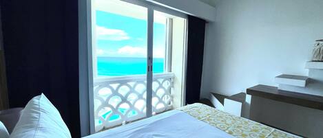 A hotel room with a bed, a small desk, and a balcony with a view of the ocean.
