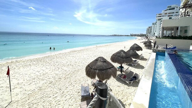 A beach resort with a swimming pool, sun loungers, and thatched umbrellas. - Ocean View Apartments (Cancun)