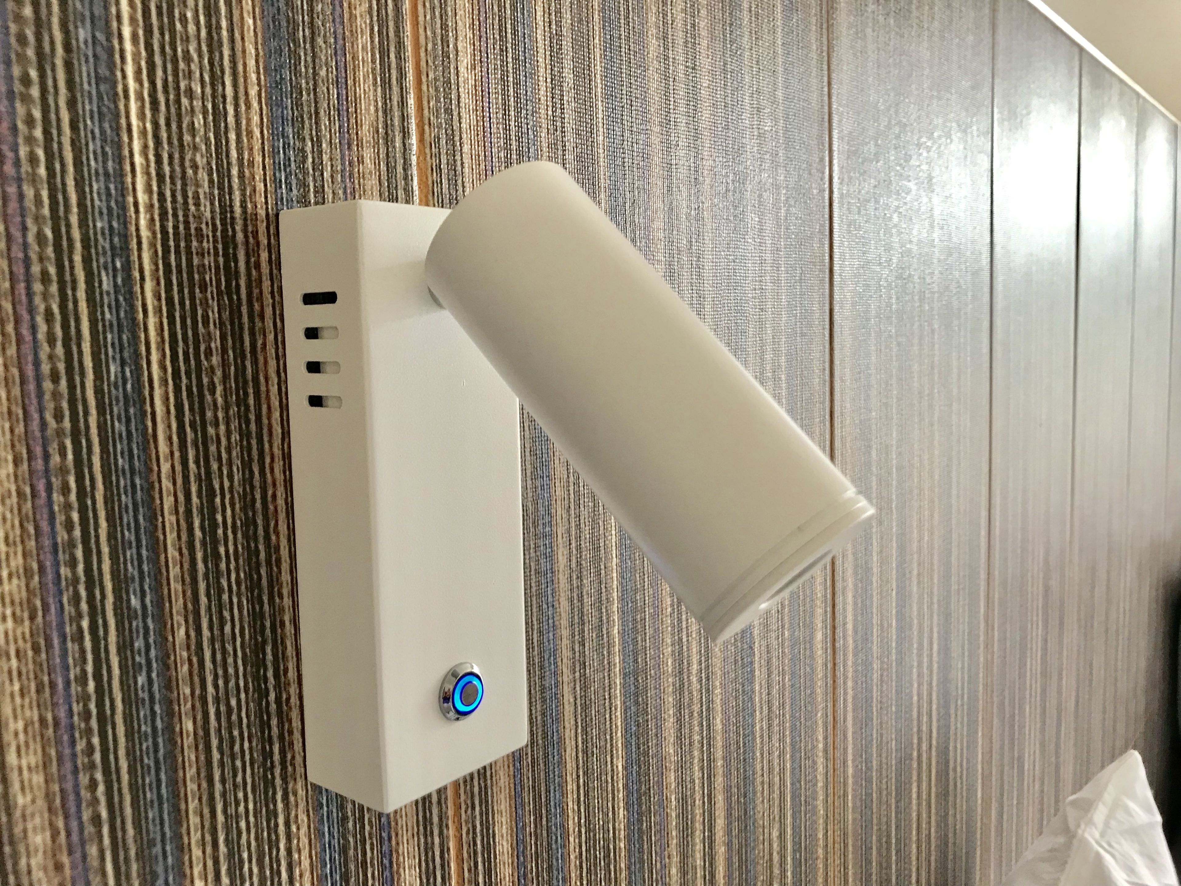 A wall-mounted device with a cylindrical attachment, possibly a sensor or light, on a textured wall.
