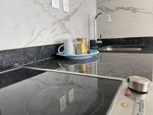 A kitchen with a black induction cooktop, a coffee maker, and a sink.