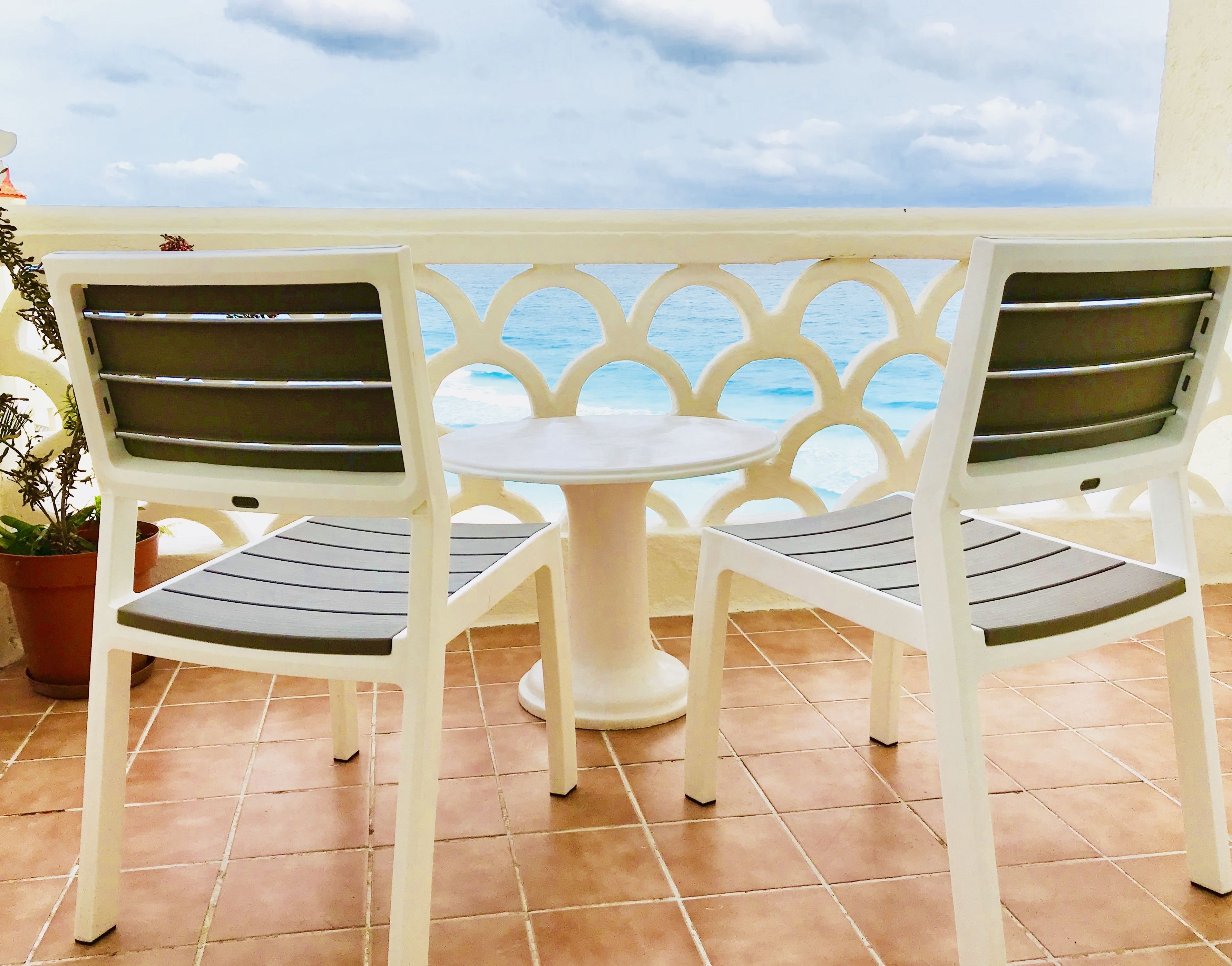 A balcony with two white chairs and a small round table, overlooking a body of water.