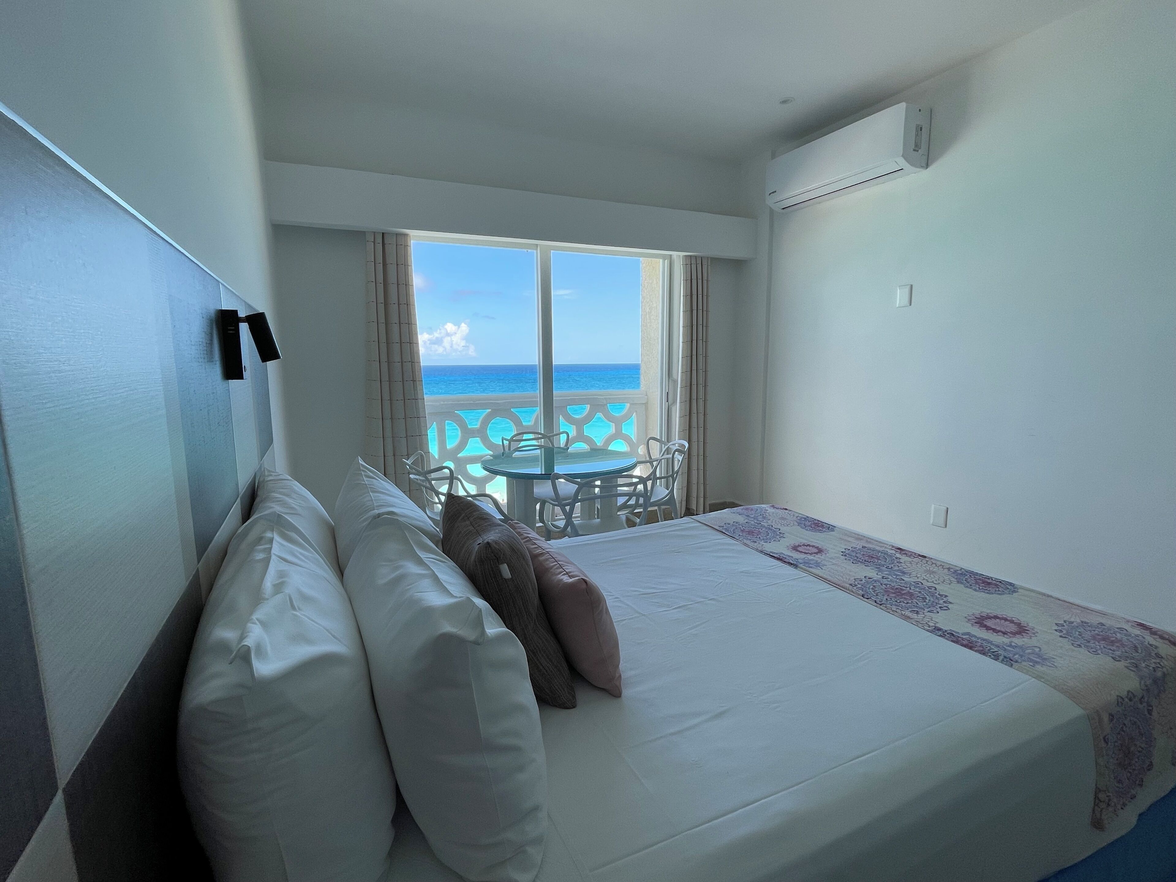A hotel room with a bed, a small table, and a view of the ocean.