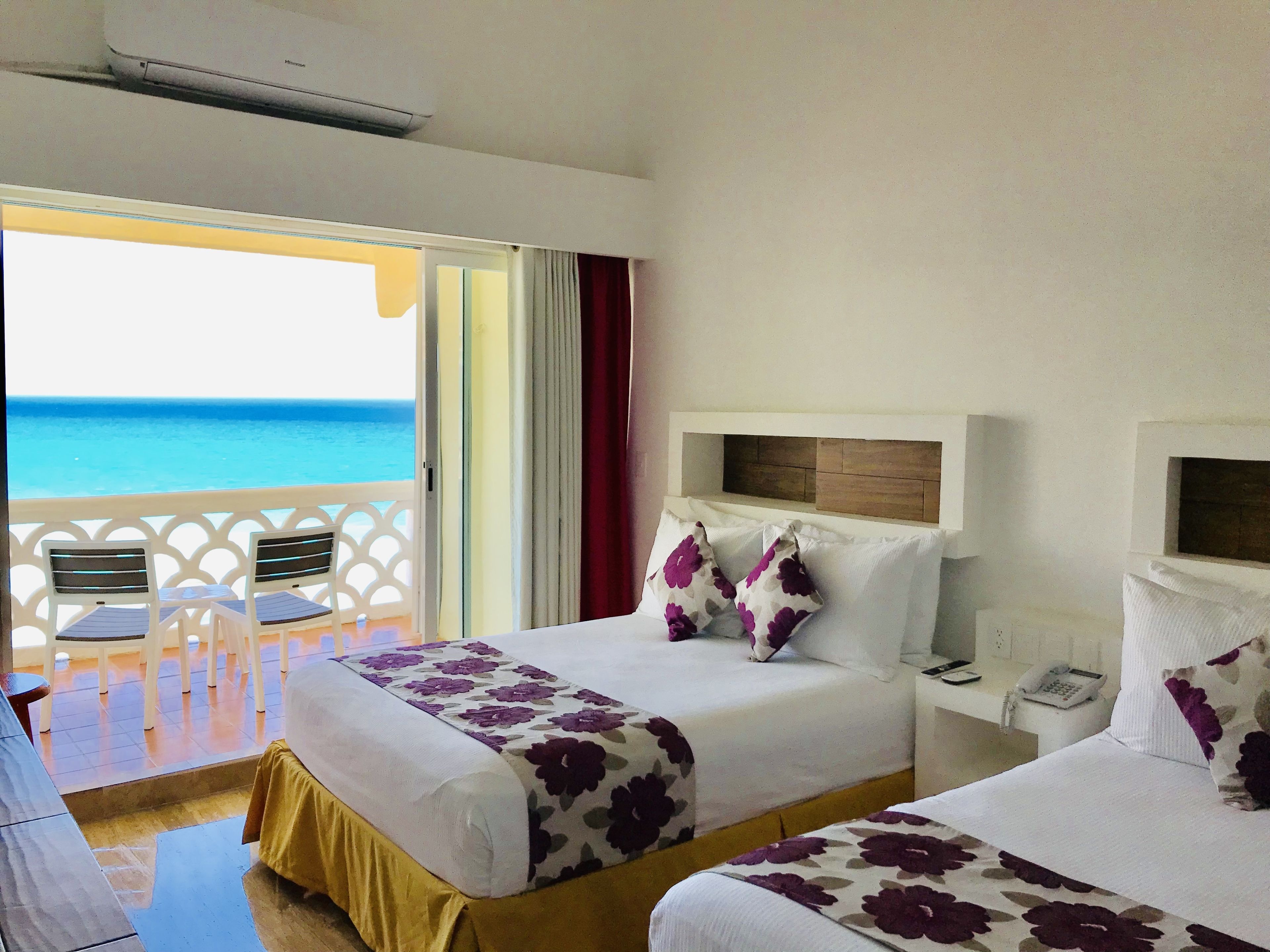 Ein Hotelzimmer mit zwei Betten, einem Balkon mit Stühlen und Meerblick.