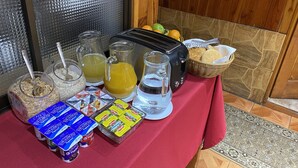 Una mesa de desayuno con cereal, jugo, agua, yogur y un tostador sobre un mantel rojo.