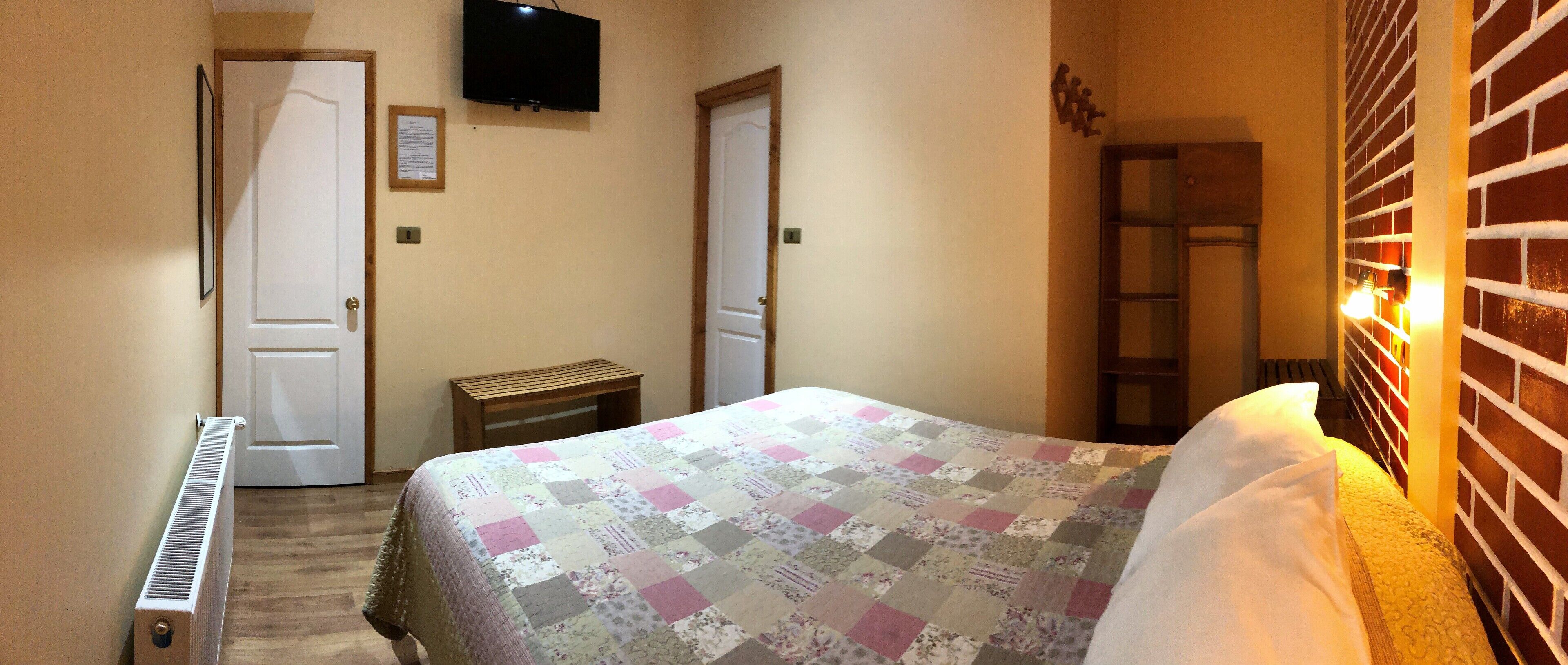 A bedroom with a bed, a radiator, a television, and a brick wall.