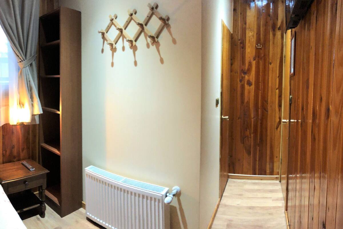 Una habitación con piso de madera, una cama, una mesita de noche, un radiador y un armario.