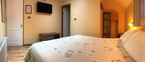 A bedroom with a bed, a television mounted on the wall, a radiator, and a door.