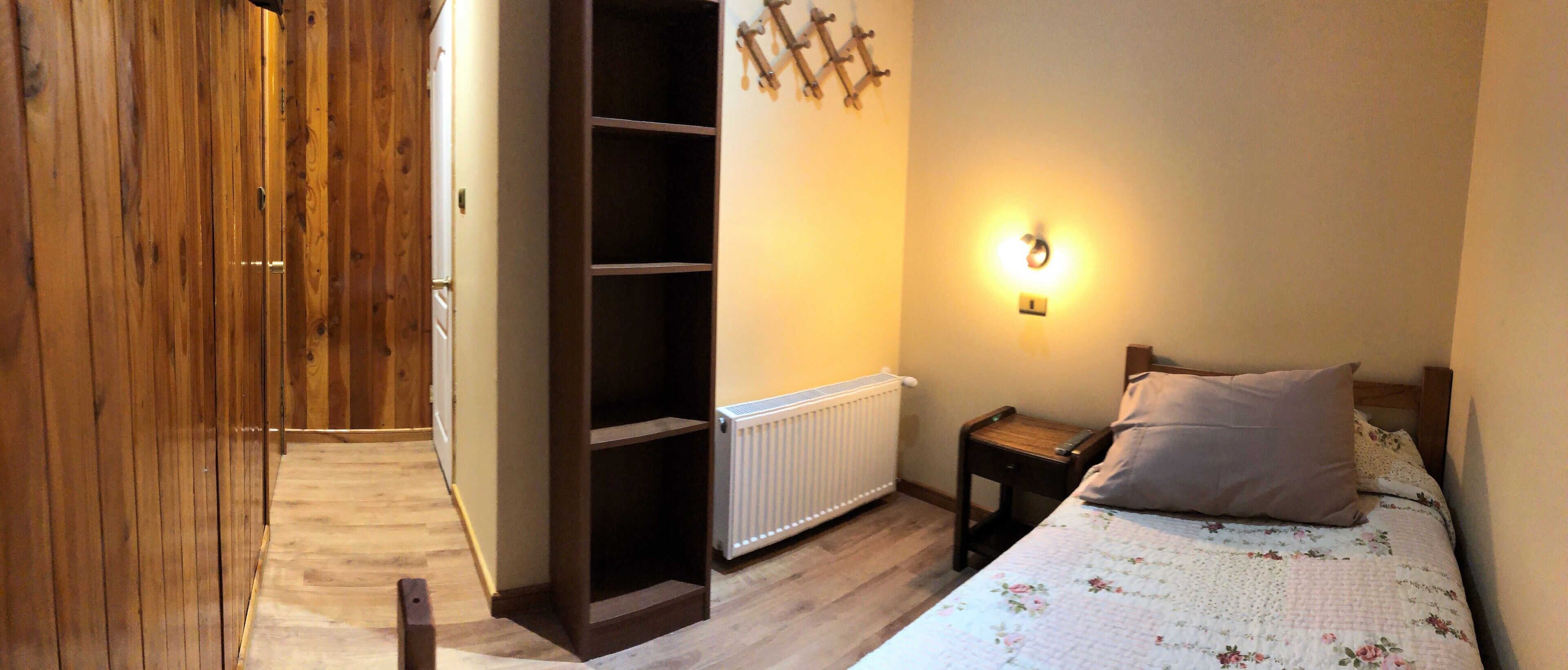 Ein Schlafzimmer mit Holzschrank, Heizkörper, Nachttisch mit Lampe und einem floralen Bettbezug.