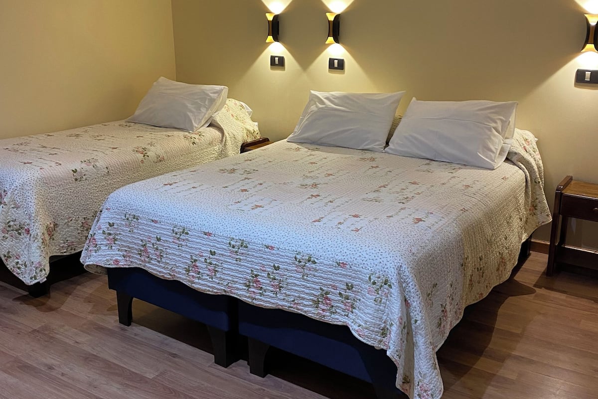 Habitación de hotel con dos camas, cada una con cubrecama estampado con motivos florales, cabeceros de madera y mesitas de noche con lámparas.