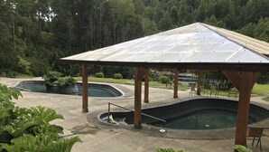 Un espacio al aire libre cubierto con dos piscinas, rodeado de vegetación y un pabellón de madera.