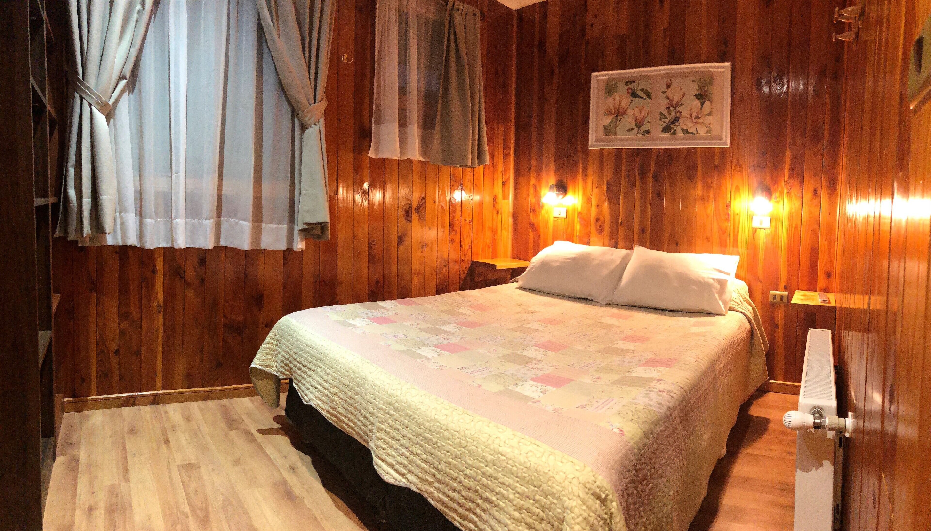 A wooden-paneled room with a bed, curtains, and a framed picture on the wall.