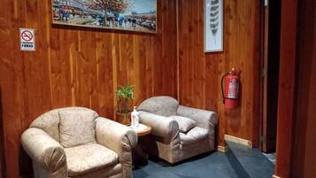 Une pièce comprenant deux fauteuils, une petite table avec une plante, un tableau, un extincteur et un panneau indiquant qu'il est interdit de fumer.