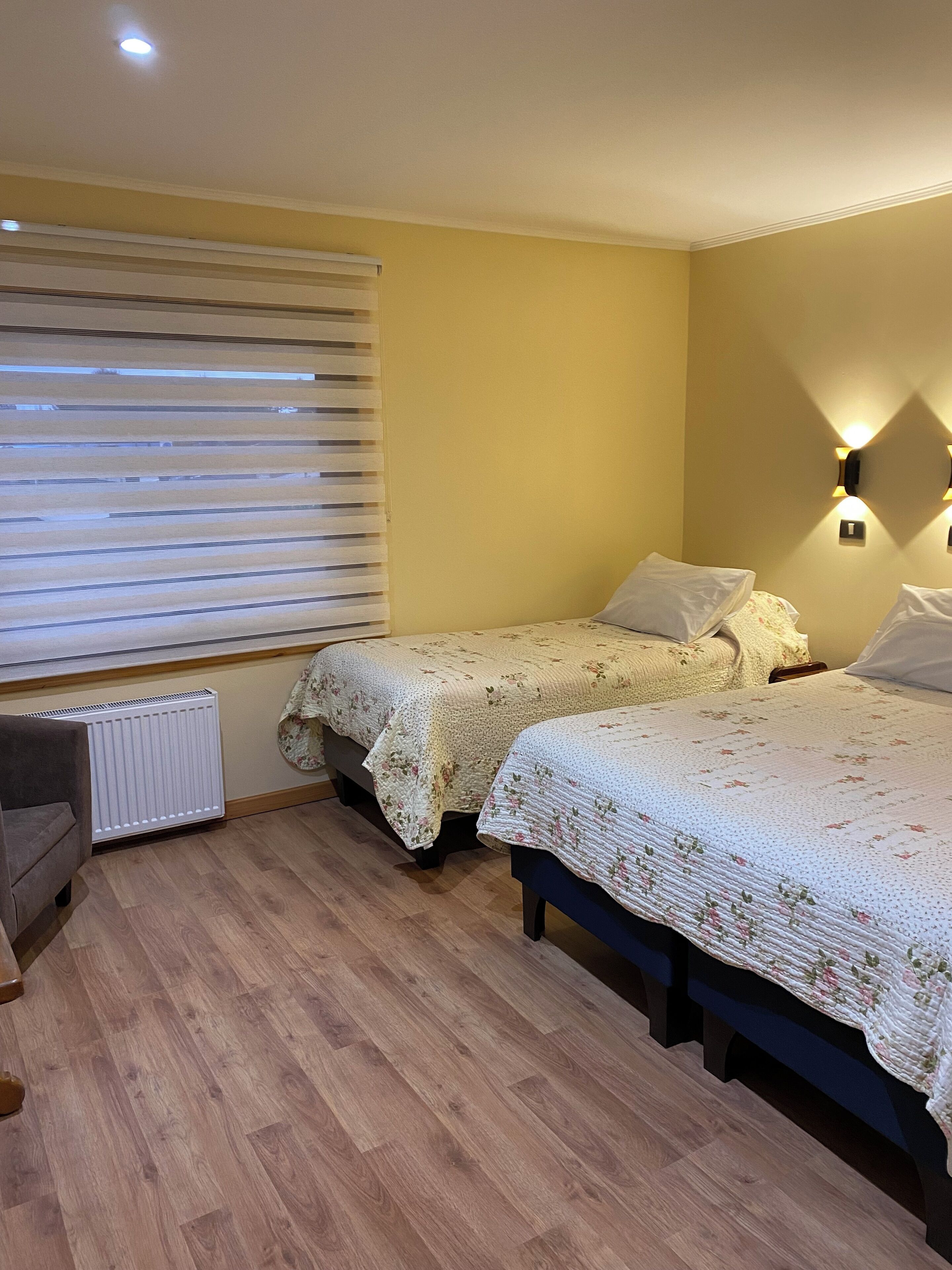 Une chambre avec deux lits, un radiateur, une chaise et une fenêtre avec des stores.