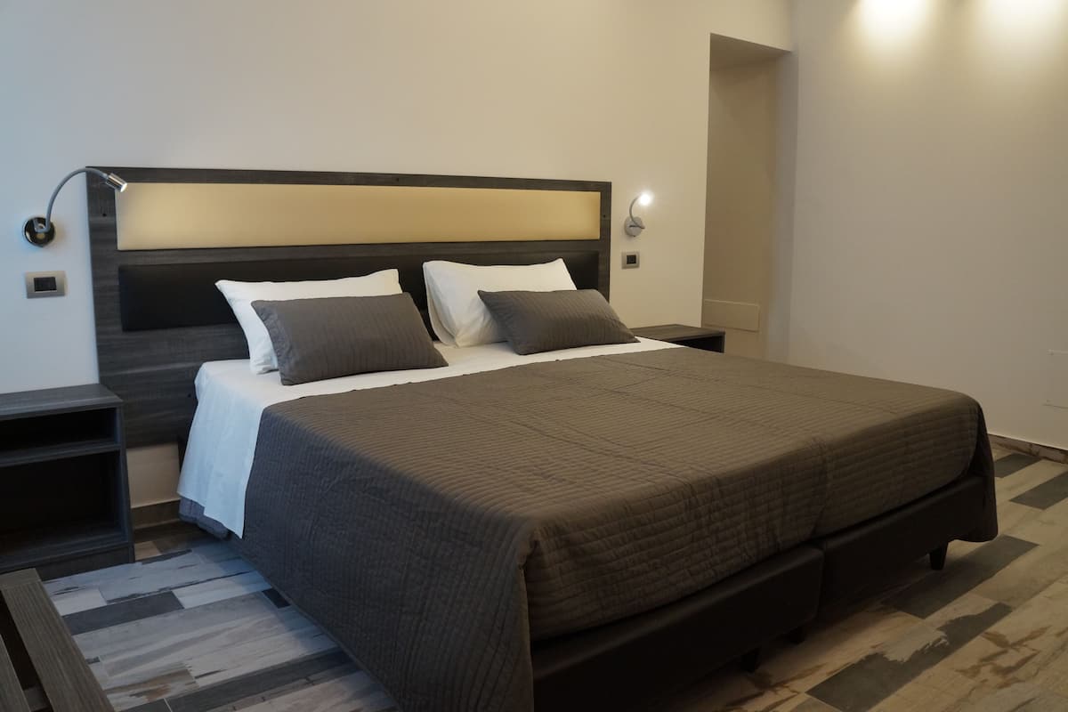 A modern bedroom with a large bed, two bedside tables, and a headboard with integrated lighting.