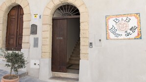 Un edificio con due porte di legno, una scala e un cartello fissato al muro con del testo.