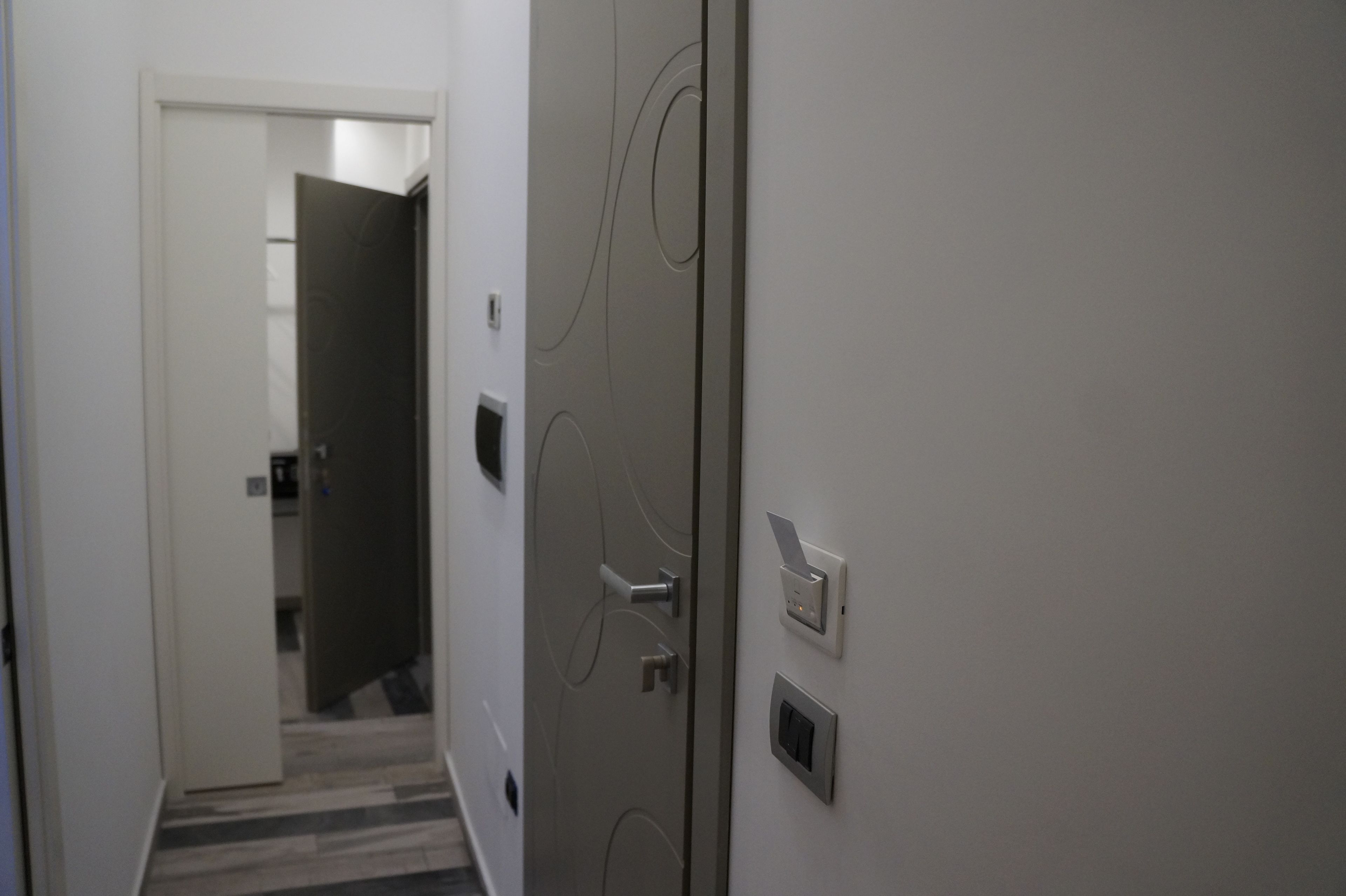 Ein Flur mit einer Tür, einem am Wand montierten Gegensprechanlage und einem Klingel.