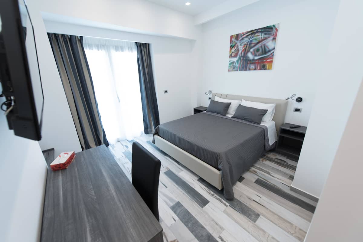 A modern hotel room with a bed, bedside tables, a desk, and a chair.