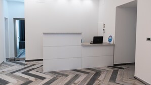 Un'area reception dal design moderno, con un pavimento a motivi a spina di pesce, una scrivania reception con un portatile e un logo al muro.