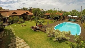 A residential area with a swimming pool, a well-maintained lawn, and a variety of plants. - Pousada Rosa da Praia (Imbituba)