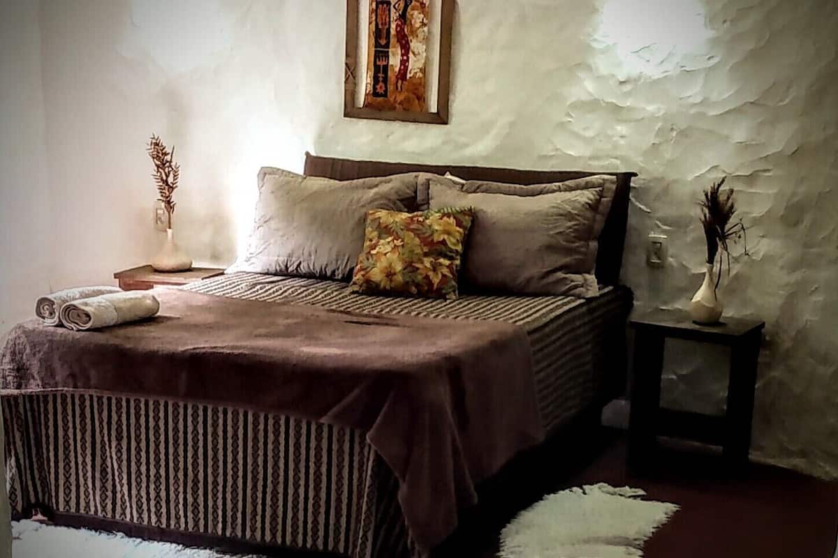 A bedroom with a bed, pillows, a nightstand, a vase, and a wall-mounted picture.