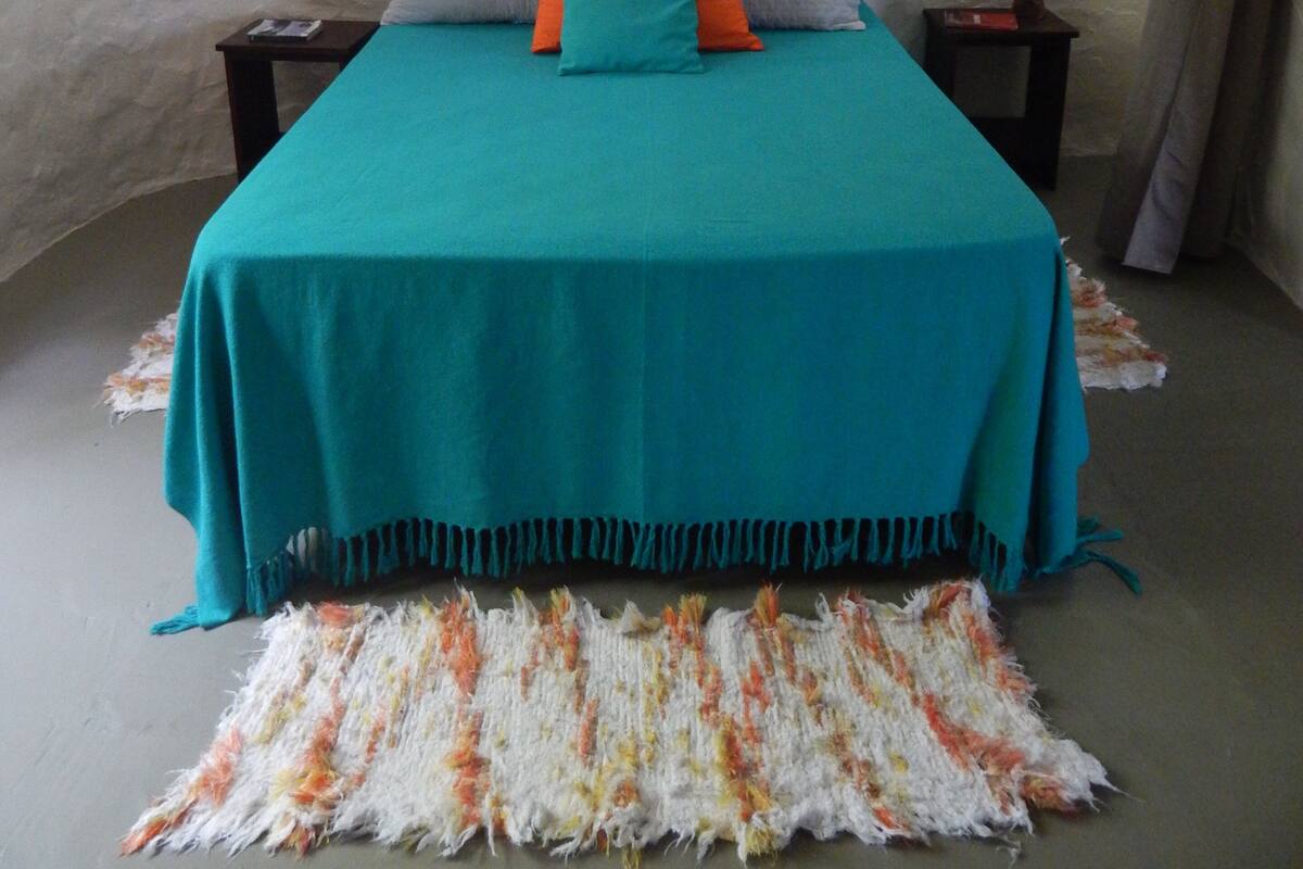 A bedroom with a teal bedspread, a heart-shaped wall decoration, and a patterned rug.