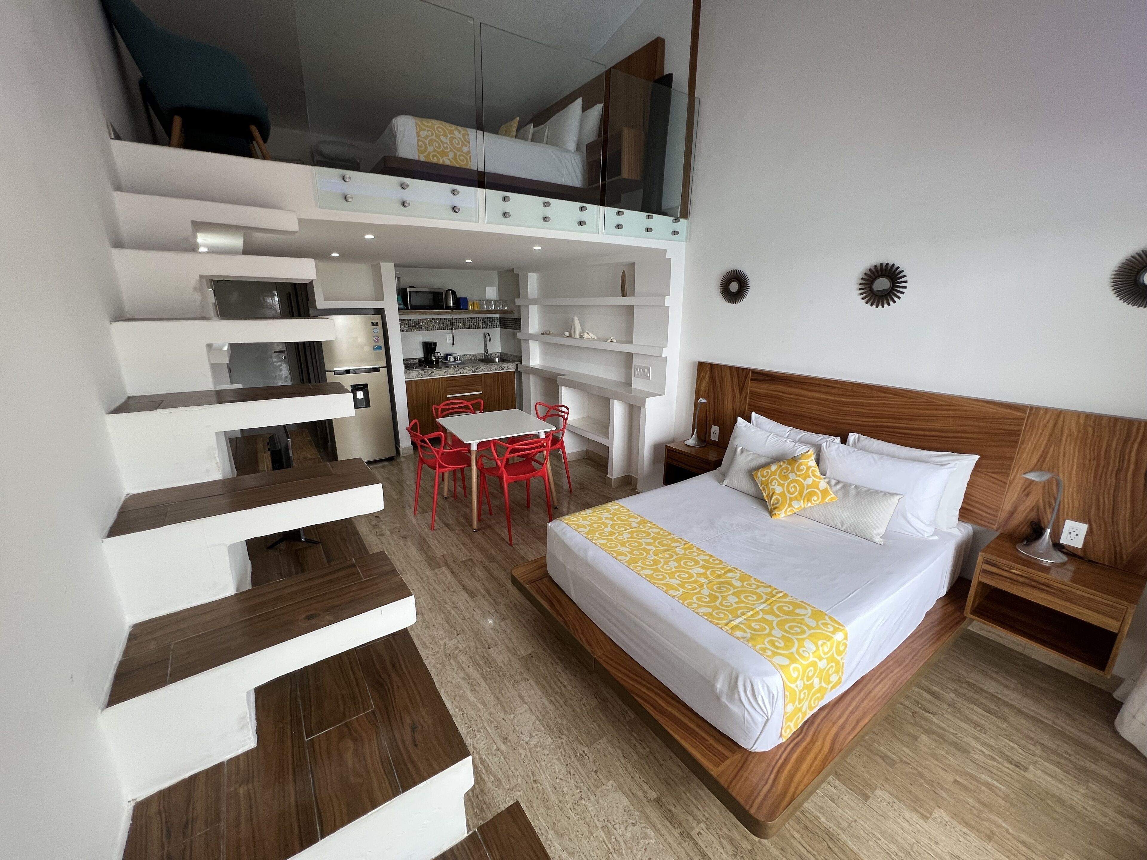Una habitación de hotel con cama, escritorio, silla, una mesita y una kitchenette.